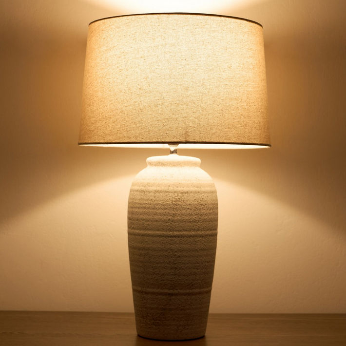 Tapered drum lamp shade lit, warm glow on ceramic base
